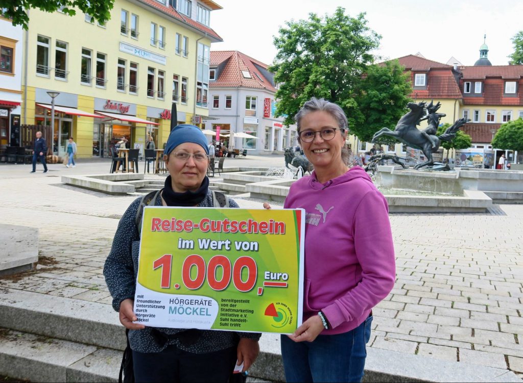 Ein freudiger Moment: Hauptgewinnerin Sylvia Scherpinski (li.) nimmt die Glückwünsche und - passend fürs Foto - den symbolischen Reisegutschein von Andrea Flörke, 1. Vorstand der Suhler Stadtmarketing Initiative, entgegen.